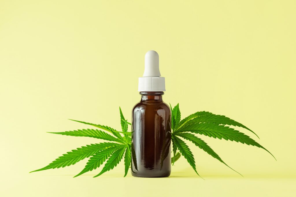 Bottle of CBD tincture, cannabis leaves, yellow background